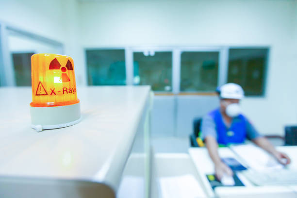 Male science researcher in protective uniform works in x-ray laboratory, ionizing radiation hazard symbol on foreground. Selective focus.