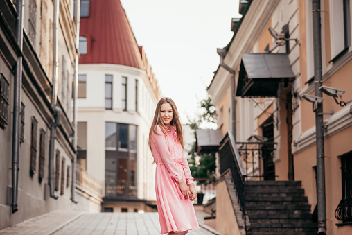 A beautiful confident girl in a pink dress, she walks through the beautiful streets of the city on a summer Sunny day, long beautiful hair, delicate makeup, urban style.