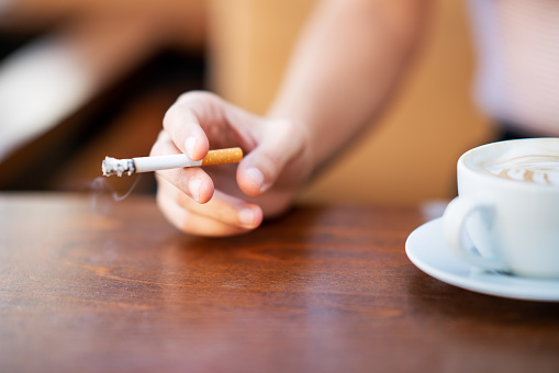 Young woman smoking and holding cup of coffee in a cafe.