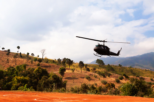 Military helicopter landing in a valley, terrace fields and mountains in the backgrounds.