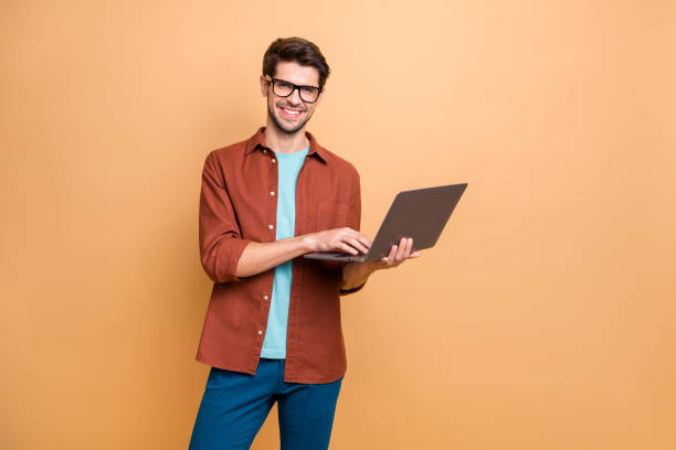 Portrait of his he nice attractive cheerful cheery successful content smart clever brunet guy agent broker holding in hands laptop working isolated over beige color pastel background Portrait of his he nice attractive cheerful cheery successful content smart clever, brunet guy agent broker holding in hands laptop working isolated over beige color pastel background netbook stock pictures, royalty-free photos & images