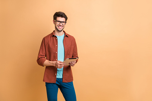 Portrait of his he nice attractive cheerful cheery successful content, brunette guy holding in hands digital e-book browsing web app isolated over beige color pastel background