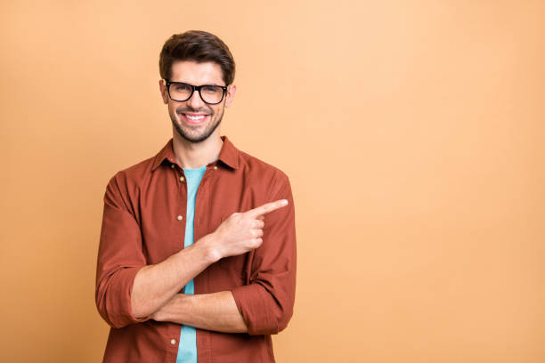 verticale de plan rapproché de son il il a agréable gaigaiement gai joyeux heureux bon type de brunet de contenu pointant l'index de côté la solution d'annonce de conseil d'isolement au-dessus du fond pastel de couleur beige - man pointing photos et images de collection