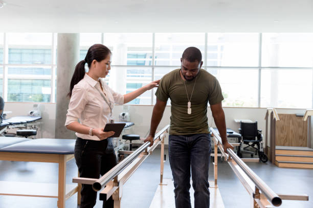 Physical therapist guides military vet as he uses injured foot The female physical therapist guides the mid adult male military veteran as he walks on his foot during therapy. veteran photos stock pictures, royalty-free photos & images