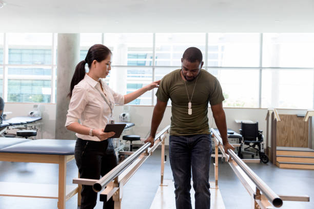 Physical therapist guides military vet as he uses injured foot The female physical therapist guides the mid adult male military veteran as he walks on his foot during therapy. military veteran stock pictures, royalty-free photos & images