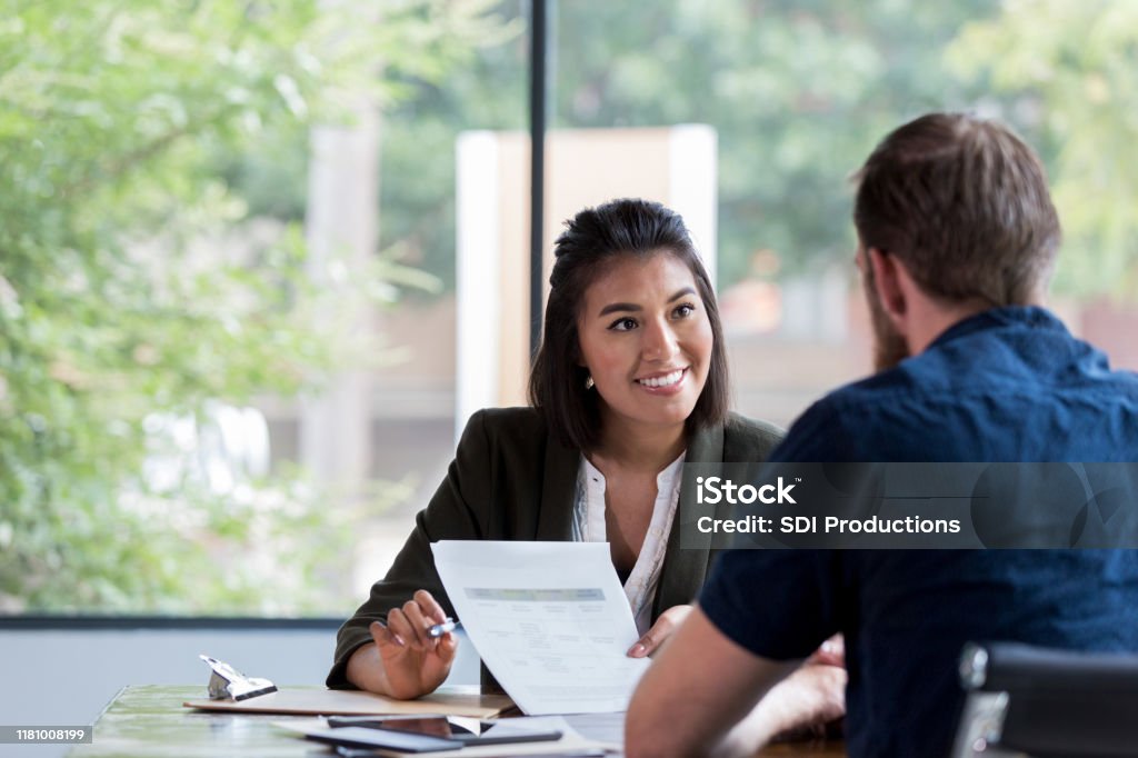 Cheerful businesswoman meets with client Hispanic businesswoman smiles while showing a document to a male associate. Advice Stock Photo