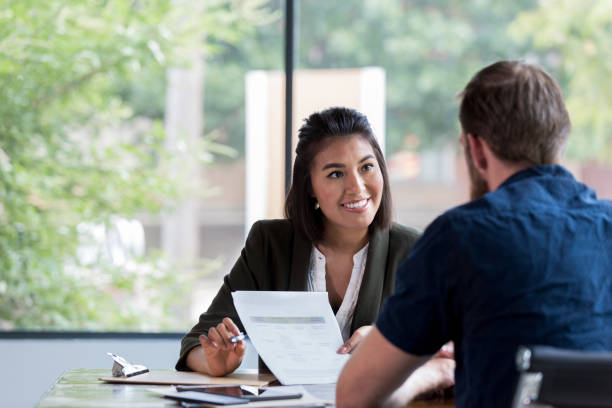 Cheerful businesswoman meets with client Hispanic businesswoman smiles while showing a document to a male associate. interview event stock pictures, royalty-free photos & images