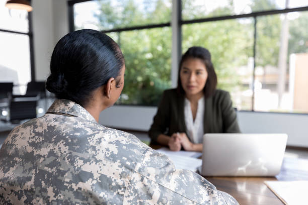 Rear view of female veteran talking with counselor Mid adult military veteran talks with a therapist. The therapist is blurred in the background. military lifestyle stock pictures, royalty-free photos & images