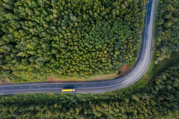 Photo of Top down aerial view of mountain road curve among green forest trees. Semi truck with cargo trailer on the highway