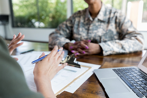 Unrecognizable female loan officer or financial advisor gestures during meeting with female military veteran.