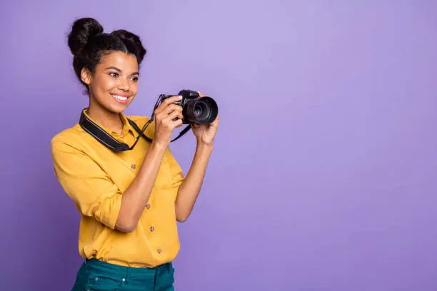 Photo of Photo of pretty dark skin lady holding photo digicam in hands photographing foreign sightseeing professional wear yellow shirt trousers isolated purple color background