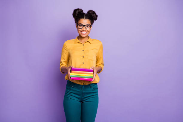 Photo of amazing high school dark skin lady holding many colorful books diligent student wear specs yellow shirt trousers isolated purple color background Photo of amazing high school dark skin lady holding many colorful books, diligent student wear specs yellow shirt trousers isolated purple color background black woman hair bun stock pictures, royalty-free photos & images