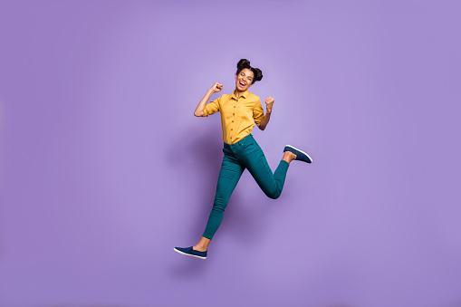 Full body profile photo of pretty dark skin lady jumping high celebrating, favorite football team victory wear casual yellow shirt trousers isolated purple color background