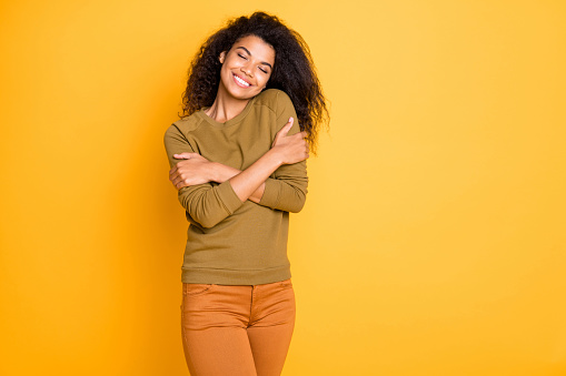 Photo of cheerful toothy beaming cute nice charming attractive black woman, wearing orange pants trousers enjoying her newly bought sweater isolated over vivid color background