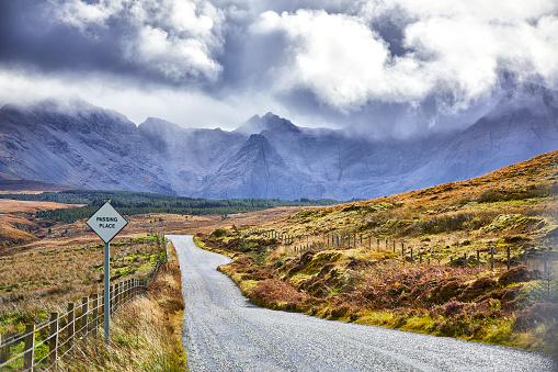 A road through a Scottish landscape near the Fairy Pools. It is cloudy but occasionally the sun breaks through the clouds.