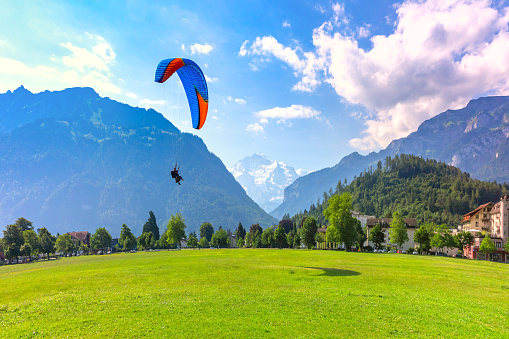 A paraglider landing at Hohematte Park in the center of Interlaken, important tourist center in the Bernese Highlands, Switzerland. The Jungfrau is visible in the background