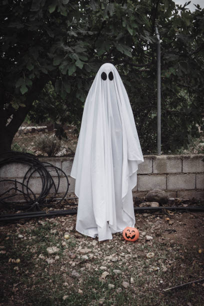 istock Ghost covered with a white ghost sheet on a forest with halloween pumpkin candy jar. 1181017132