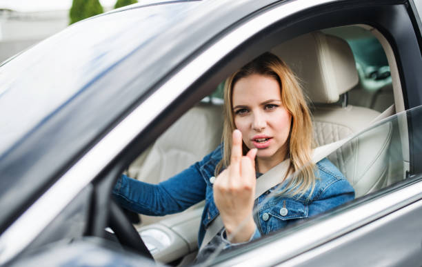 chauffeur fâché de jeune femme s'asseyant dans la voiture, affichant le doigt moyen. - long blond hair photos et images de collection