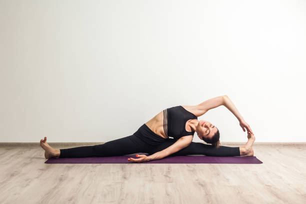 retrato cheio do comprimento da mulher adulta nova nas calças pretas e na ioga toppraticando, no situação em divisões e em fazer a cabeça girava em torno ao exercício para diante do joelho, pose do sirsasana do janu do parivrtta - gymnastics the splits teenage girls stretching - fotografias e filmes do acervo