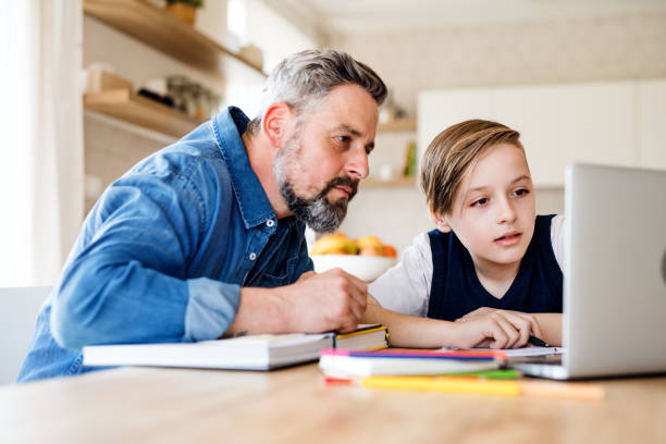 Mature father with small son sitting at table indoors, using laptop.