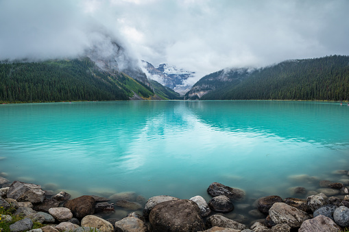 Turquoise-colored Lake Louise with reflections of the surrounding mountains on a foggy day, Banff National Park, Alberta, Canada