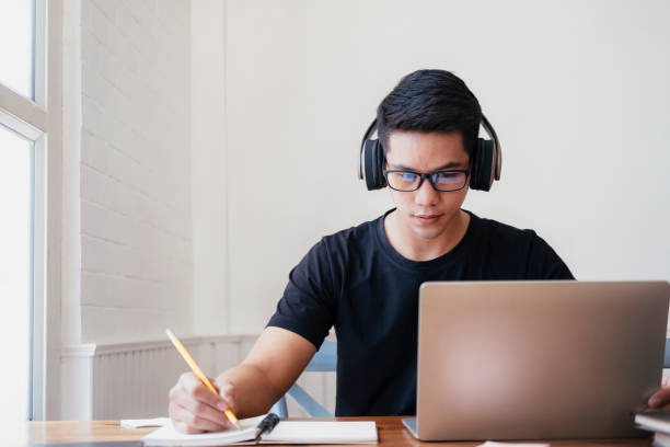 estudo do estudante do homem novo em casa usando o portátil e aprendendo em linha. - online university - fotografias e filmes do acervo