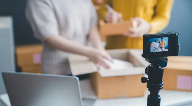 Photo of Beautiful asian woman blogger showing clothes in front of camera to recording vlog video live streaming at her shop. Business online influencer on social media concept. Online Selling. Online Shopping