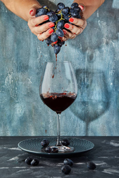 istock Female hands squeezing grapes into a glass with wine, on a blue background. Wine production concept 1181030857