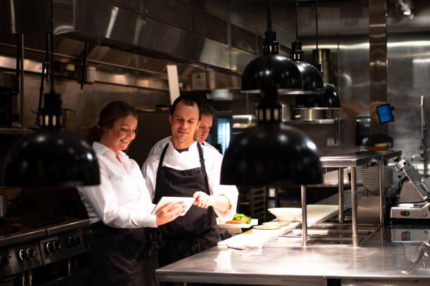 Hospitality team discussing bookings on a tablet Chefs and restaurant manager discussing reservations. Foodservice and hospitality workers. Restaurant staff working. waiter stock pictures, royalty-free photos & images