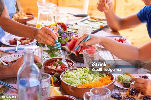 Group Of Caucasian Hands On The Wooden Table Mix Of Vegetables Salad And Spinach Meatballs Fresh Fruits And Drink Stock Photo - Download Image Now