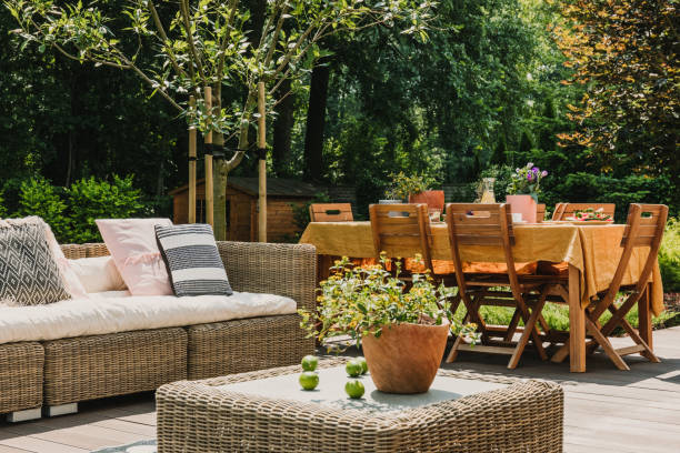 istock Green pant on wicker coffee table in front of Dining table covered with orange tablecloth standing on wooden terrace in green garden 1181034167