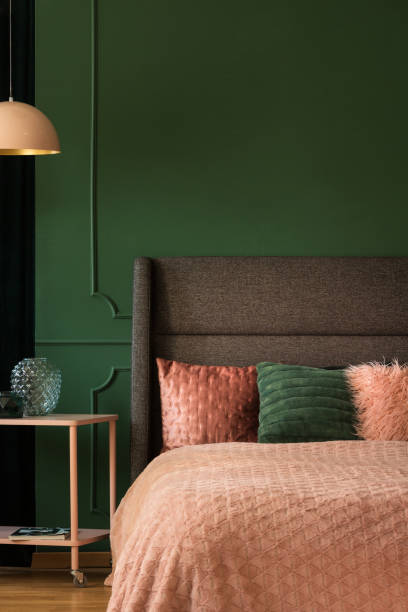 istock Pastel pink and emerald bedding on comfortable king size bed with headboard, copy space on empty wall 1181034678