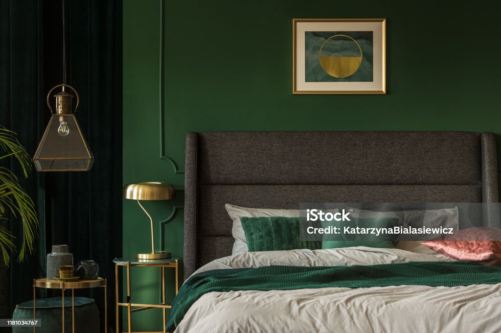 Stylish emerald green and golden poster above comfortable king size bed with headboard and pillows in dark green bedroom Bedroom Stock Photo