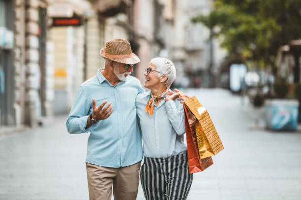 przystojny starszy mężczyzna i jego piękna żona na ulicach miasta z papierowymi torbami - women walking shopping street zdjęcia i obrazy z banku zdjęć