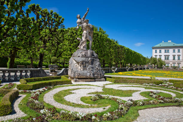 Salzburg, Austria - March 31, 2024: Mirabell gardens with Roman and Greek statues, Mirabell Palace and St. Andrä parish church on the background