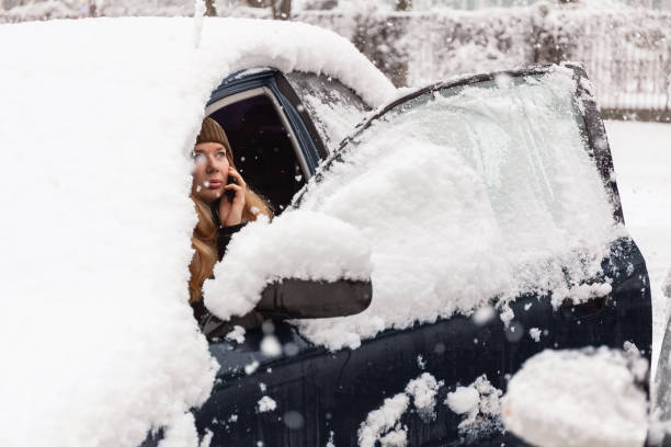 istock Young woman calling for help or assistance inside snow covered car.  Engine start in frost. Breakdown services in the winter 1181039124