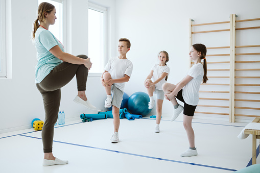 Young trainer and group of kids warming up before sport classes
