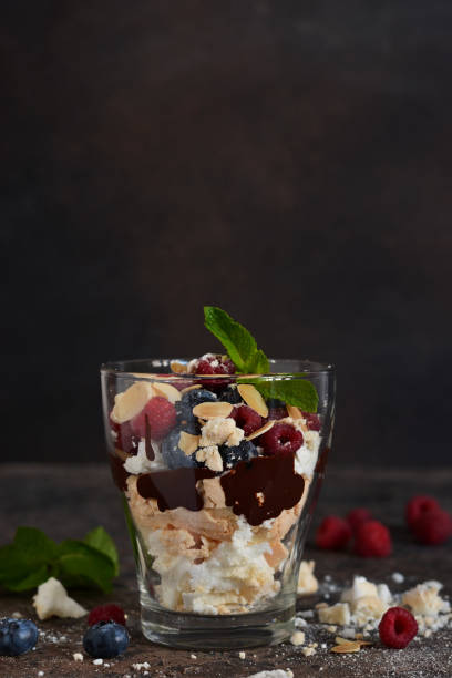 Dessert in a glass with chocolate, meringues and berries on a dark background. Close up view. Dessert in a glass with chocolate, meringues and berries on a dark background. Close up view. yogurt fruit biscotti berry fruit stock pictures, royalty-free photos & images