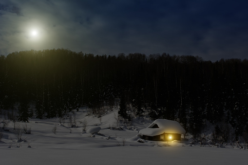 Lonely wooden house in Siberian mountains covered with a lot of fresh snow. Ski tour chalet. Abandoned cottage in winter forest at night. Christmas winter night. Shelter's Ward in deep wild thicket.