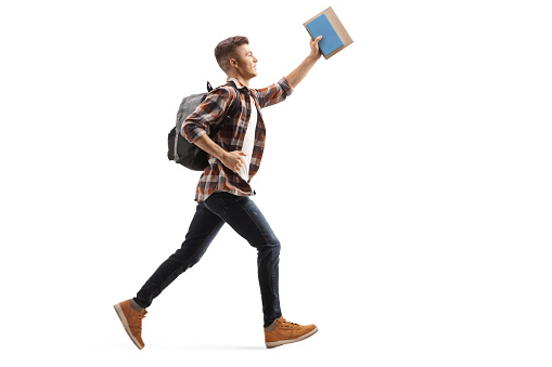 Full length profile shot of a male student running and holding a book isolated on white background