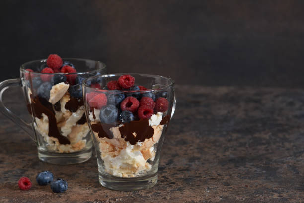 Dessert in a glass with chocolate, meringues and berries on a dark background. Close up view. Dessert in a glass with chocolate, meringues and berries on a dark background. Close up view. yogurt fruit biscotti berry fruit stock pictures, royalty-free photos & images