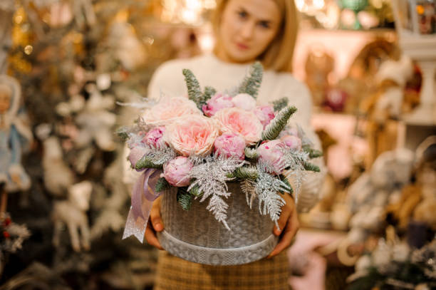 istock Woman holding a grey sweater pattern box with light pink peony roses decorated with fir-tree branches 1181048105