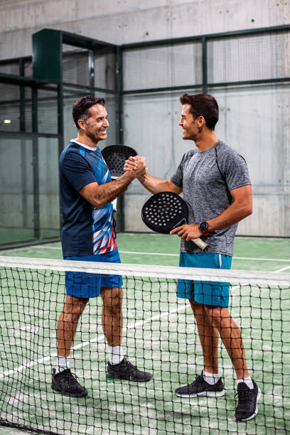 dos jugadores de pádel estrechando las manos después de ganar un partido de pádel - tennis court tennis net indoors fotografías e imágenes de stock