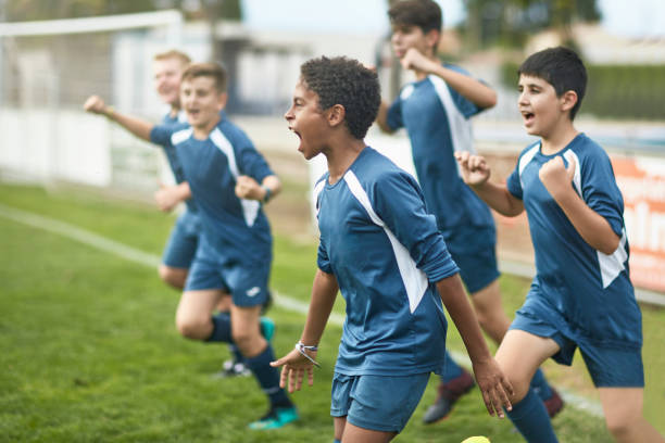 Team of Confident Young Male Footballers Running Onto Field Energetic preteen and teenage male footballers cheering and punching the air as they run onto field for training session. soccer field photos stock pictures, royalty-free photos & images