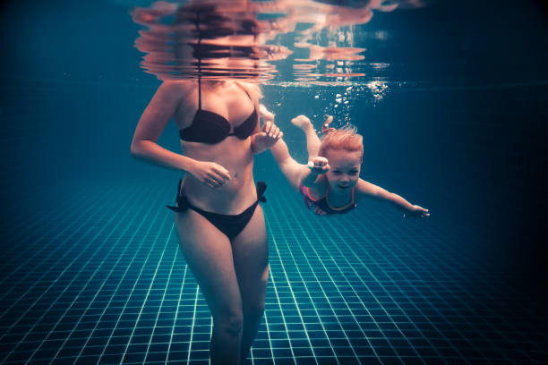 istock Happy child learning swimming underwater in swimming pool during diving training course with helping mother 1181065160