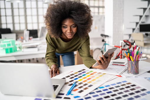 Fashion designer working in studio. Young black woman in an office smiling to camera, close up