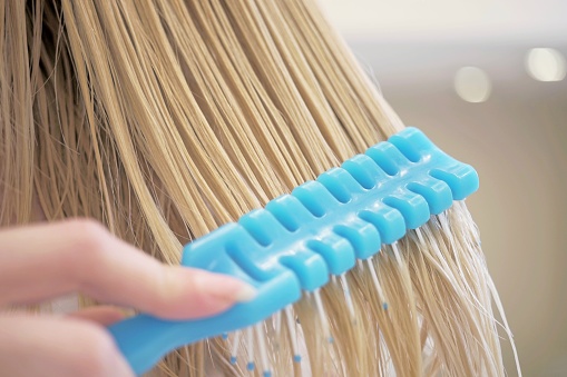 combing wet blonde hair with a blue comb, close-up.