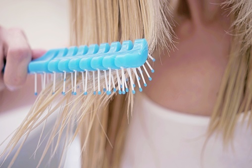 young girl combing her wet blond hair with a blue comb, close-up.