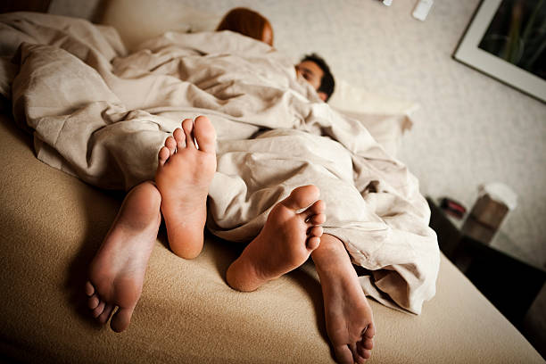 Couple in bed with feet hanging out the covers stock photo