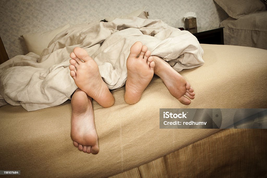 Pareja en la cama con las patas de montaje de cubiertas - Foto de stock de Comportamiento sexual humano libre de derechos